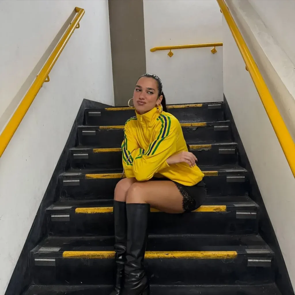 Dua Lipa com Jaqueta do Brasil, botas pretas de cano alto e short preto